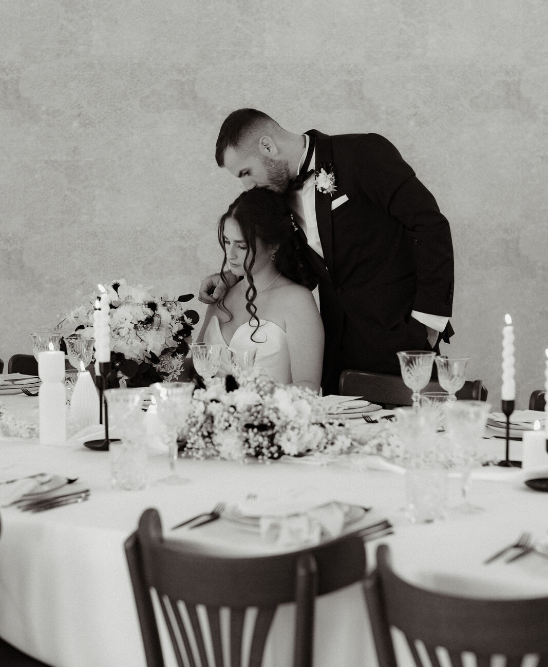 Braut sitzt an Tafel Bräutigam steht daneben