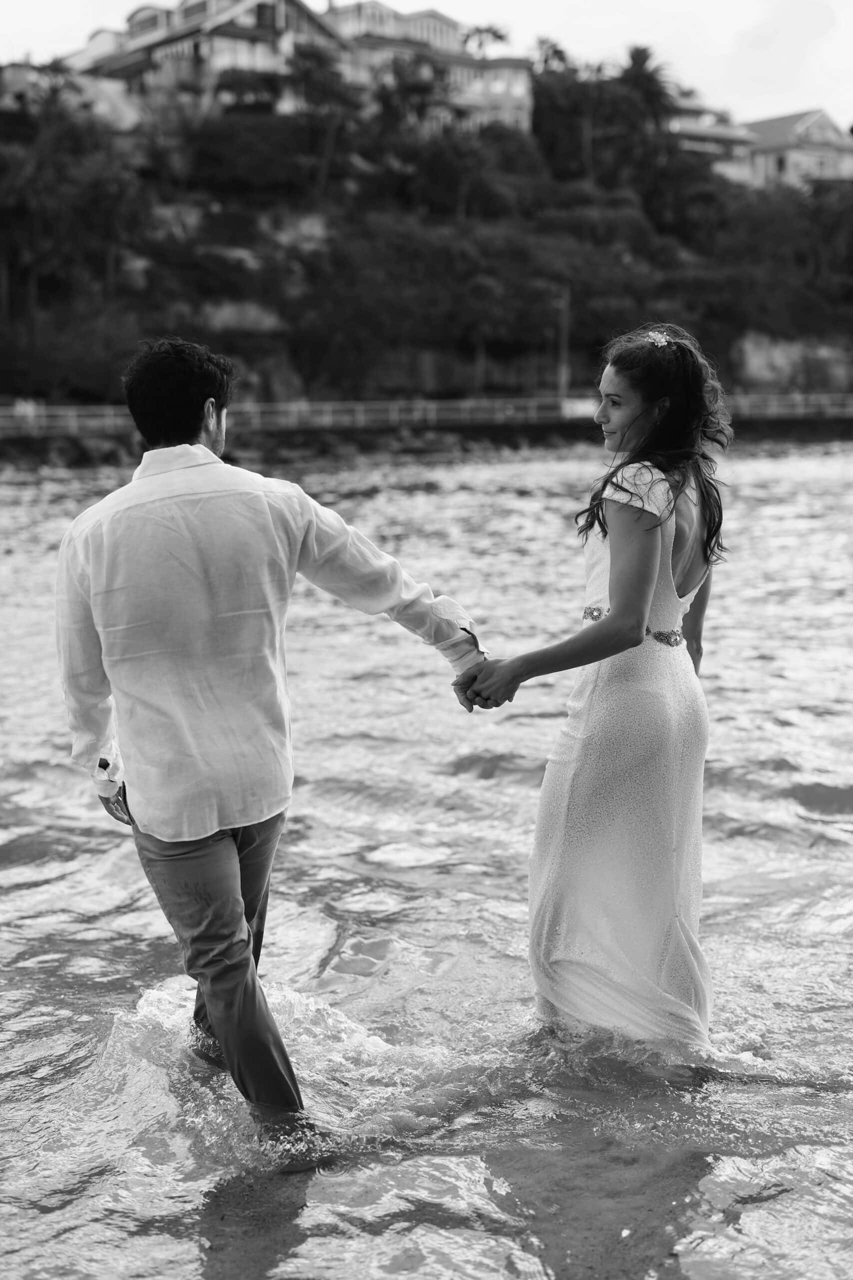 Couple walking hand in hand through water during elopement